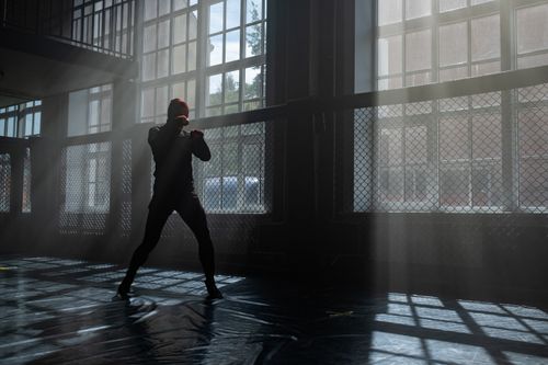 Free A silhouette of a fighter practicing boxing in a gym with dramatic sunlight streaming through the windows. Stock Photo