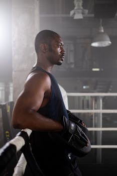 A determined boxer with focus mitts stands in a boxing ring, exuding strength and readiness.