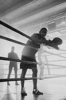 Black and white image of a boxer resting in the ring during training.
