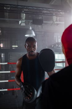 Focused boxing trainer holds pads for athlete in a gym setting.