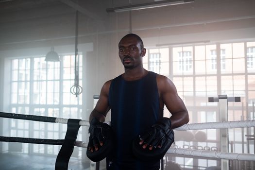 Determined boxer standing in a boxing ring, ready for training indoors.