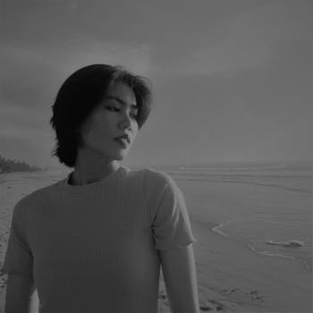 Black and white portrait of a woman standing on the beach with calm waves.
