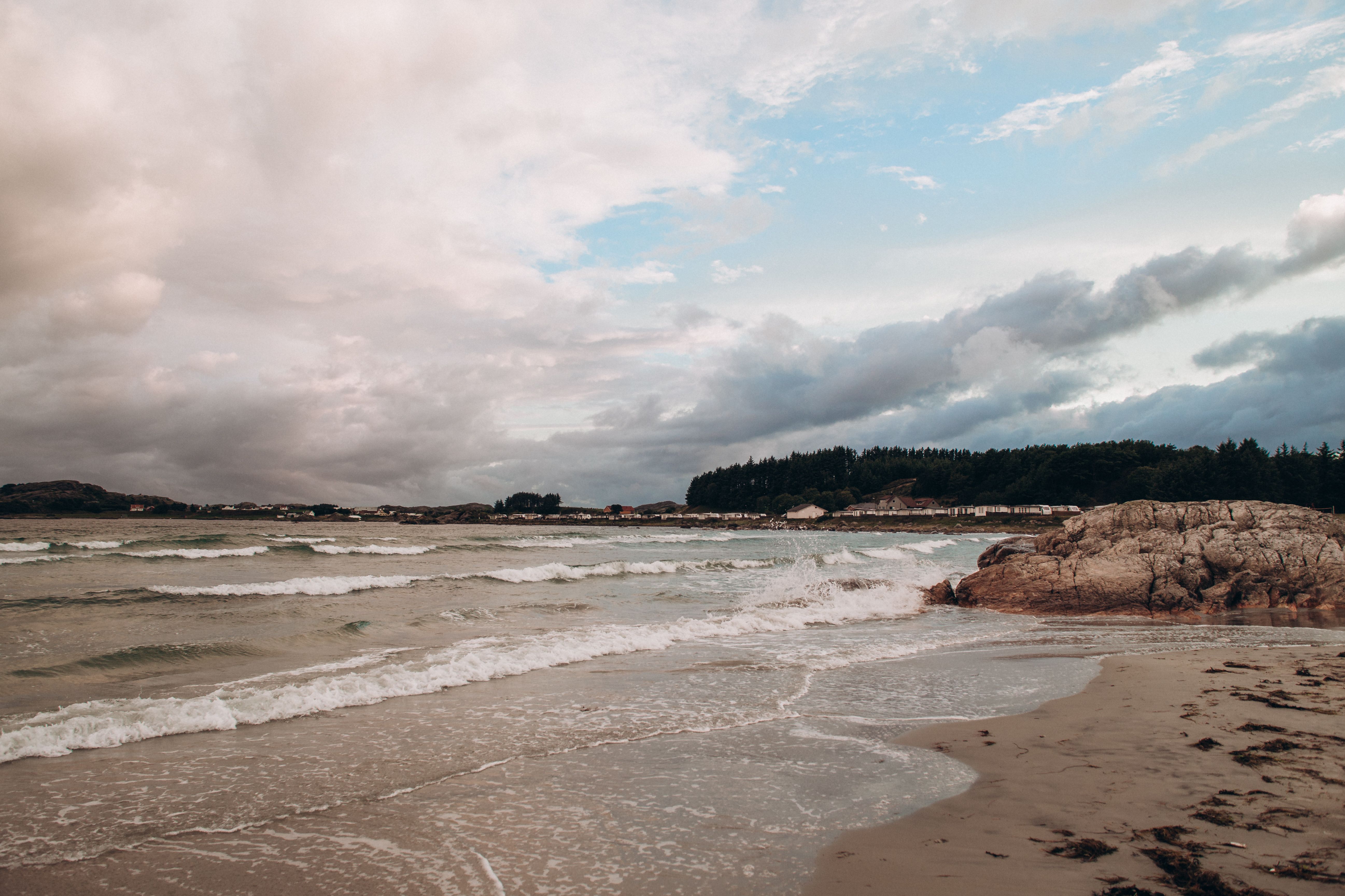 Serene beach in Norway with gentle waves and rocks under a cloudy sky, a perfect coastal landscape.