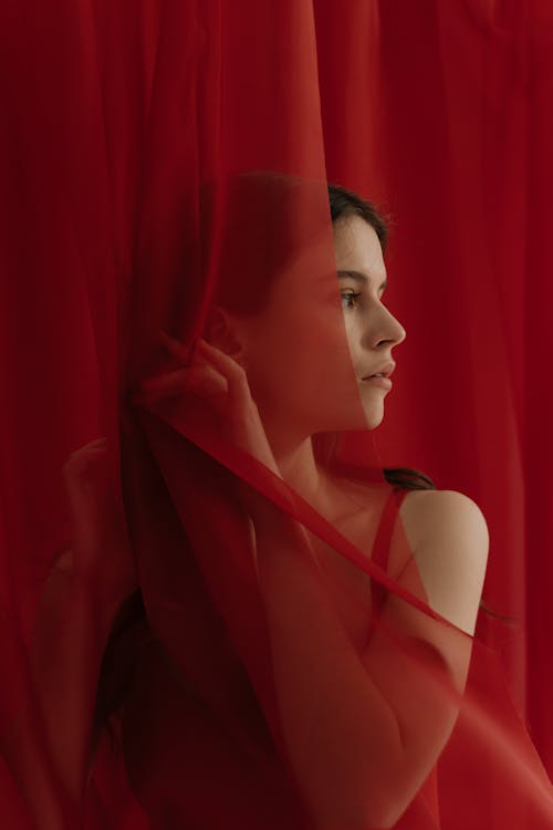 Girl in Red Spaghetti Strap Top Standing Near A Red Curtain
