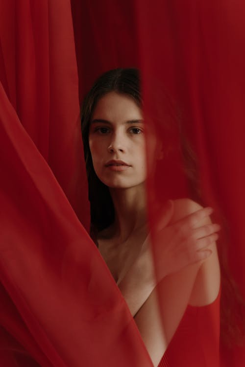 Young Woman Standing Behind A Red Sheer Curtain Fabric