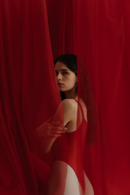 Woman in Red Bathing Suit Standing Behind a Curtain