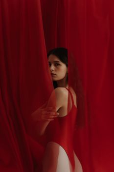 Artistic portrait of a woman posing in a red swimsuit, behind sheer red curtains.