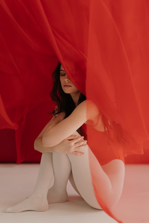 Young Woman In Red Swimsuit Sitting Behind A Red Sheer Curtain Fabric