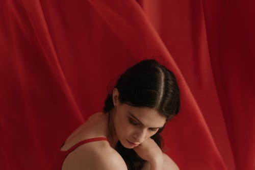 Woman in Red Spaghetti Strap Top Sitting Near A Red Curtain