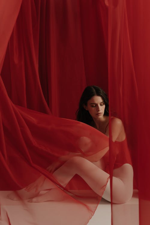 Woman Sitting Behind A Red Sheer Curtain Fabric