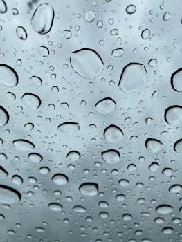 Close-up of raindrops on glass with a cloudy sky background.