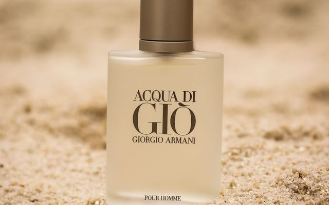 A bottle of Acqua di Giò Pour Homme standing in warm sand