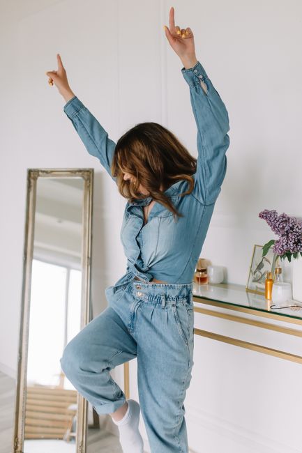 A carefree woman in denim dances energetically indoors, expressing joy and freedom.