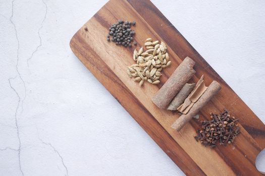 Flat lay of aromatic spices including cinnamon, cloves, cardamom, and peppercorns on a wooden cutting board.