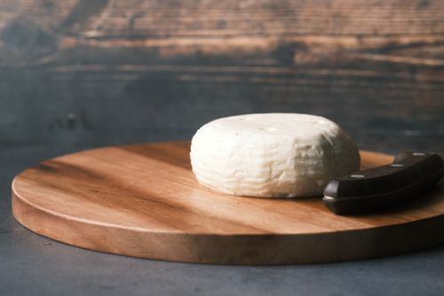 Free Round cheese on a rustic wooden board with a knife, depicting simplicity and gourmet appeal. Stock Photo