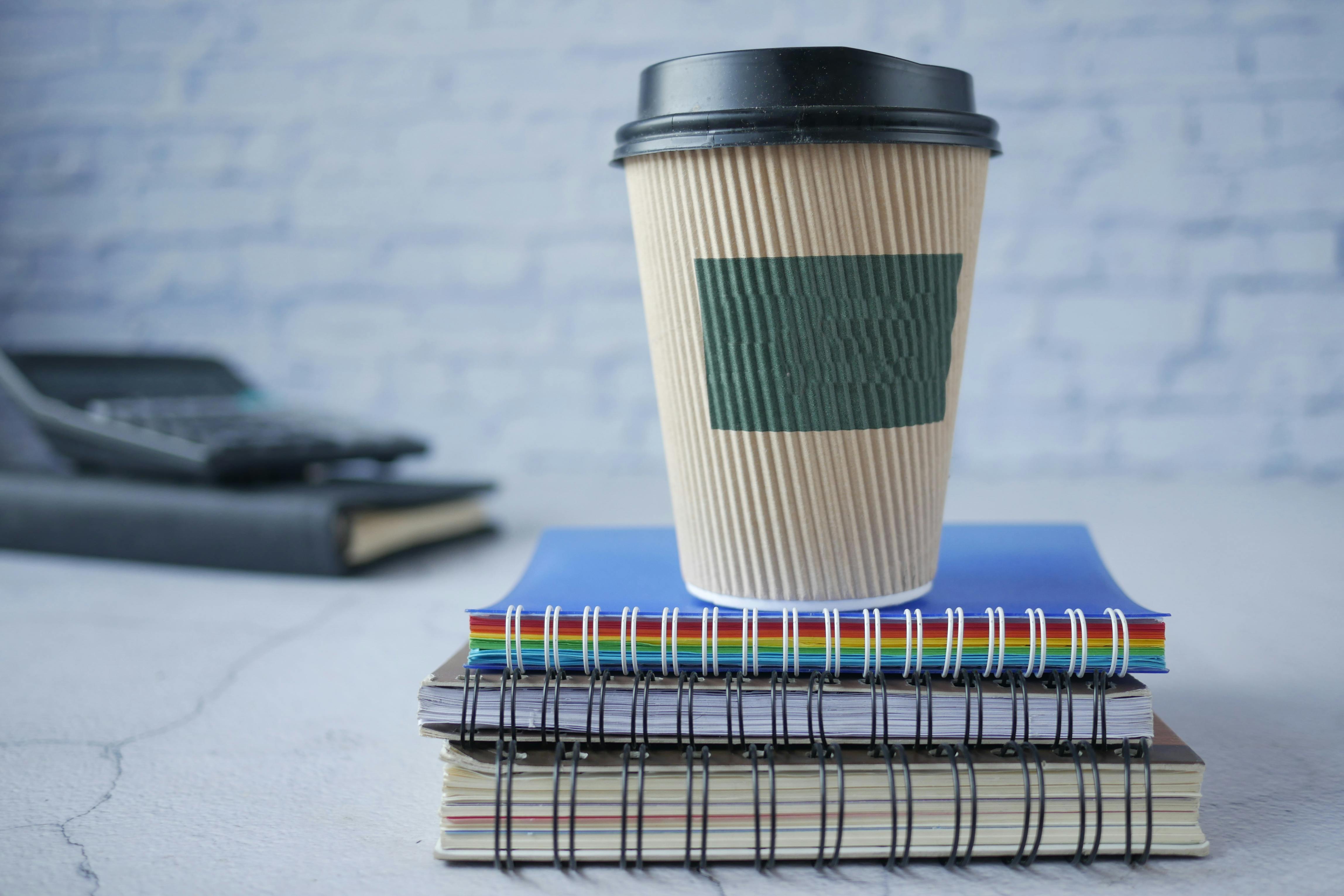A disposable cup on stacked spiral notebooks, perfect for branding mockups.