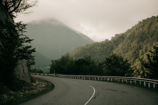 A winding road through misty mountains and lush greenery captures serene nature.