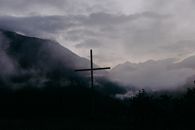 Silhouette of Cross on Green Grass Field Near Mountain Under White Clouds