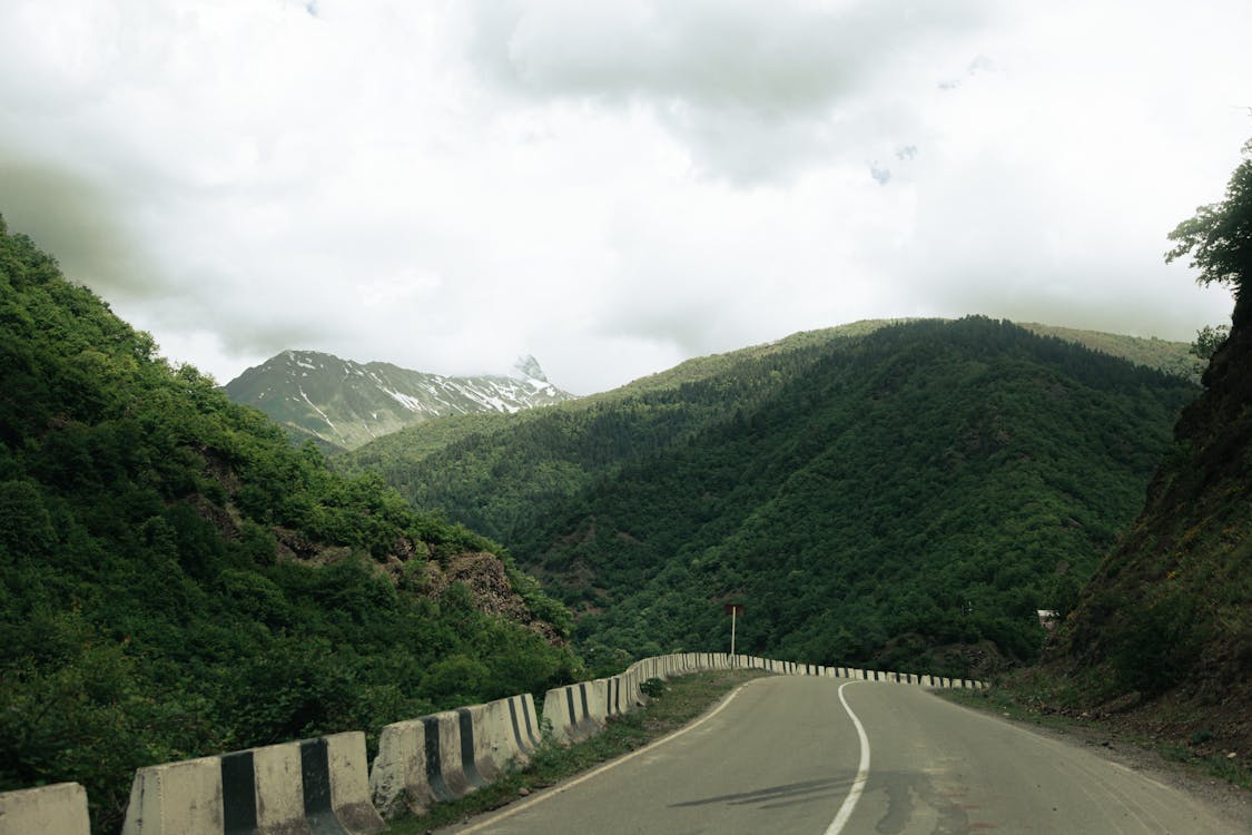 Road Between Green Mountains Under White Cloudy Sky