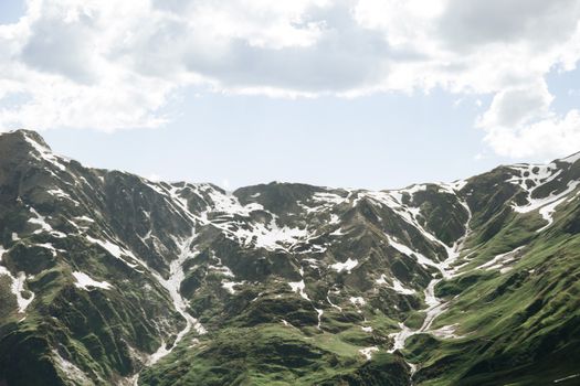 Breathtaking view of snow-dotted mountains under a cloudy sky, showcasing the beauty of nature.