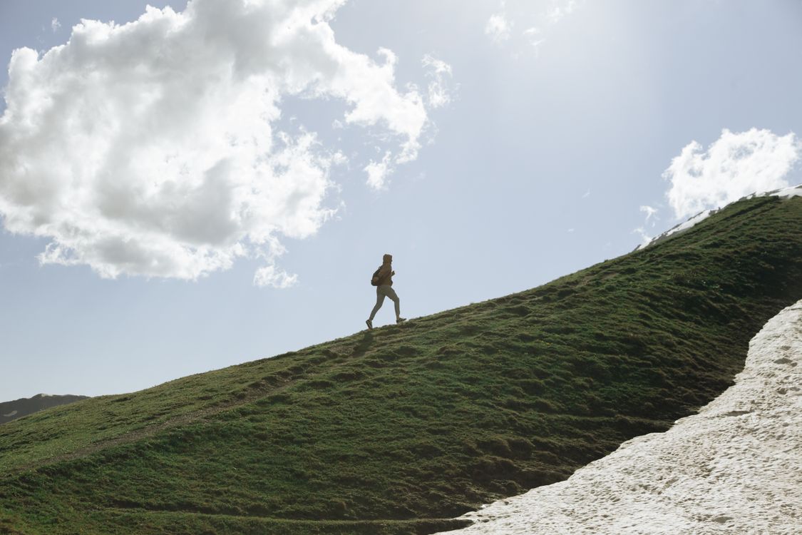 Person Walking on Green Grass Field Under White Clouds · Free Stock Photo