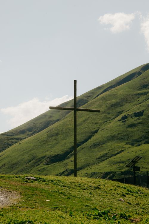 Free Peaceful rural scene with a wooden cross on lush green hills under a bright sky. Stock Photo