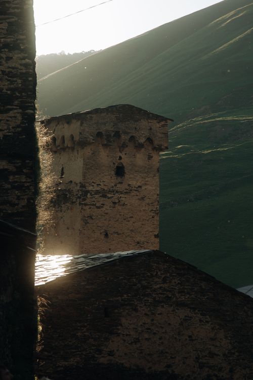 Free A medieval stone tower bathed in early morning light amidst lush green hills. Stock Photo