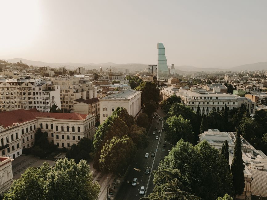 Aerial view of Tbilisi, Georgia, showcasing urban landscape and modern skyscraper at sunset.