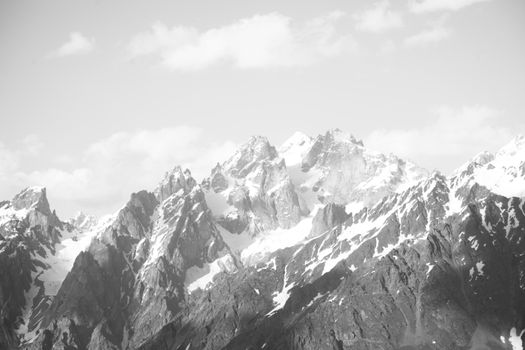 A dramatic black and white photograph of craggy, snowcapped mountain peaks.