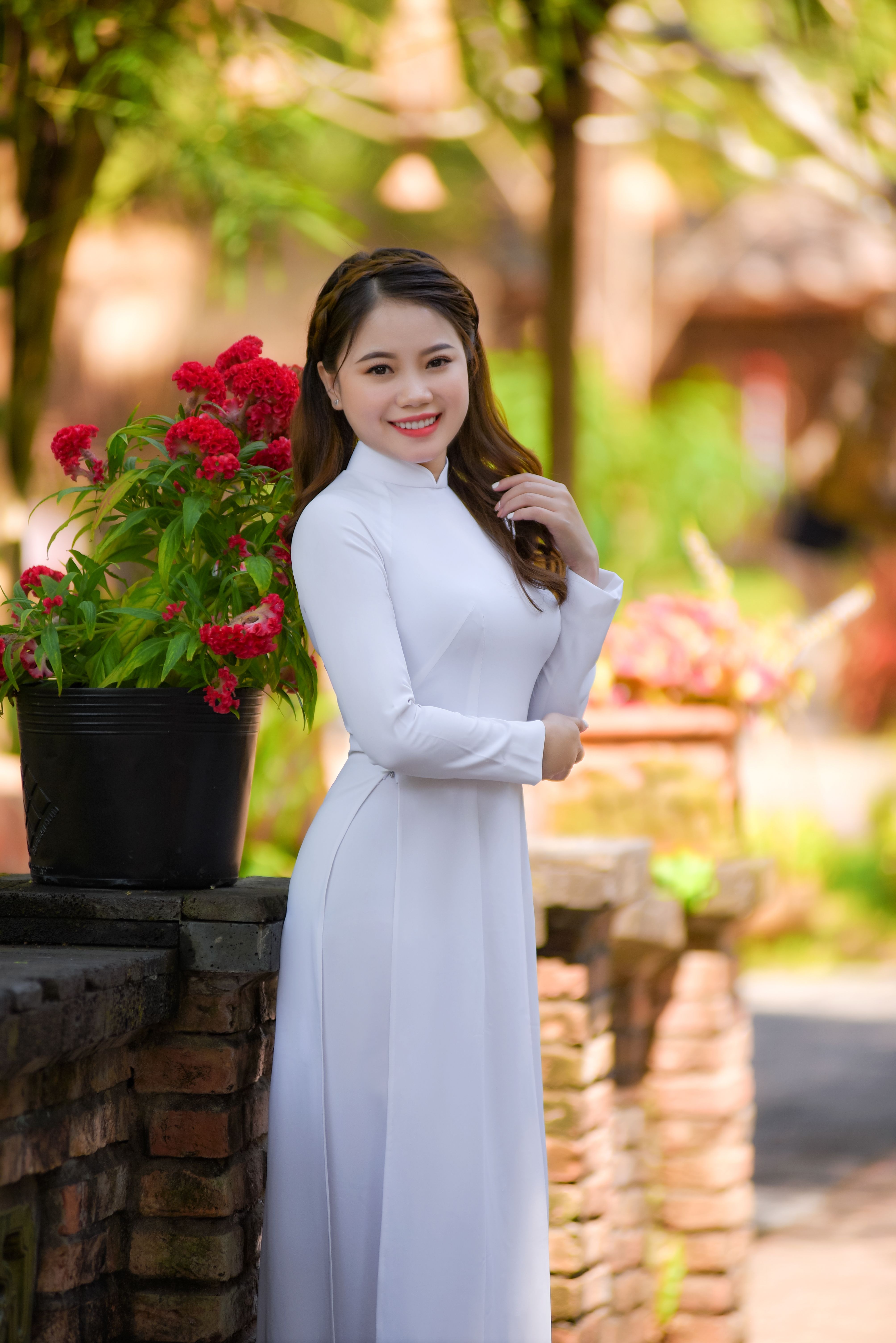 Beautiful Asian woman in a traditional ao dai smiling outdoors among flowers.
