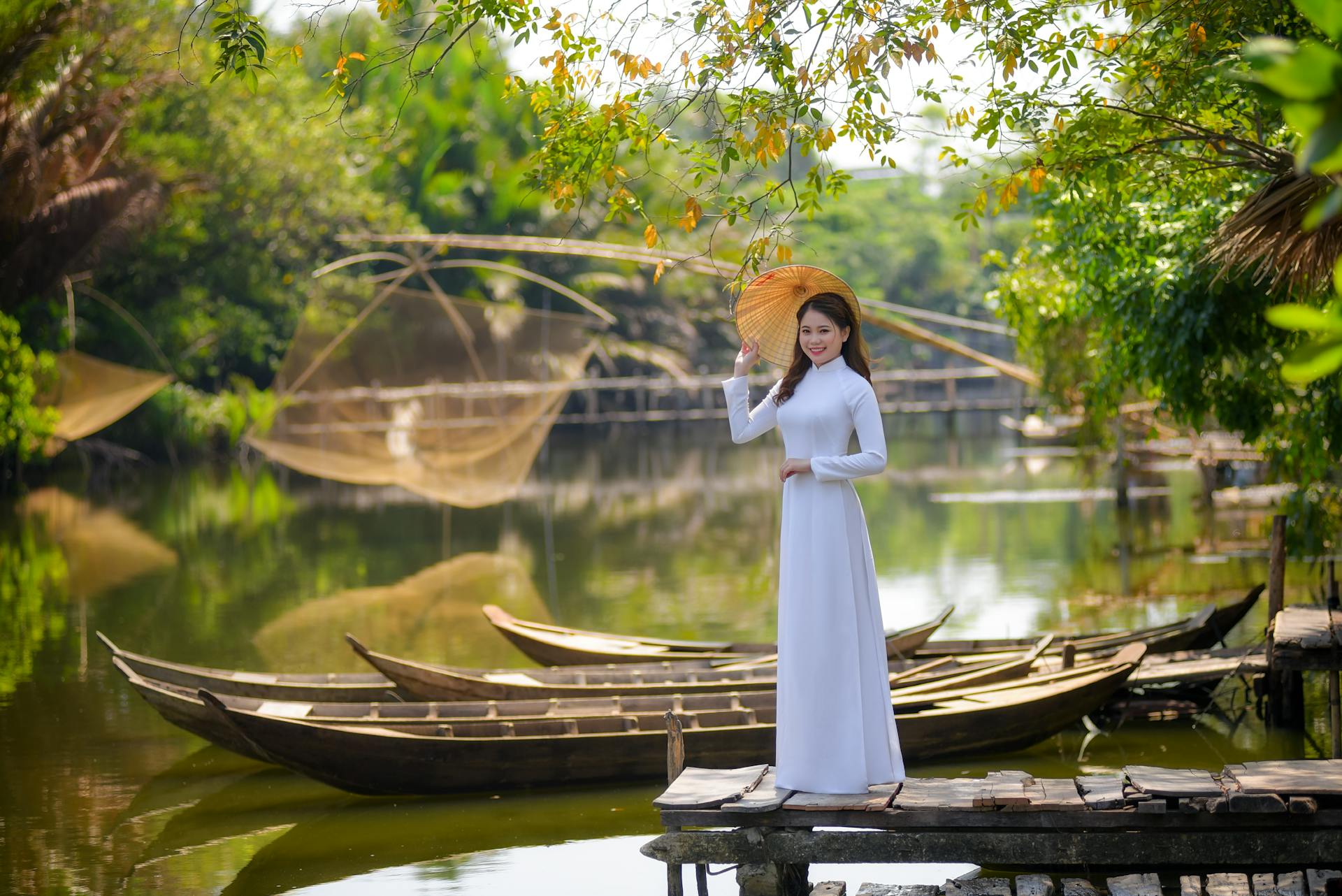Elegant Vietnamese woman in traditional Ao Dai holding a conical hat by a serene river in Vietnam.