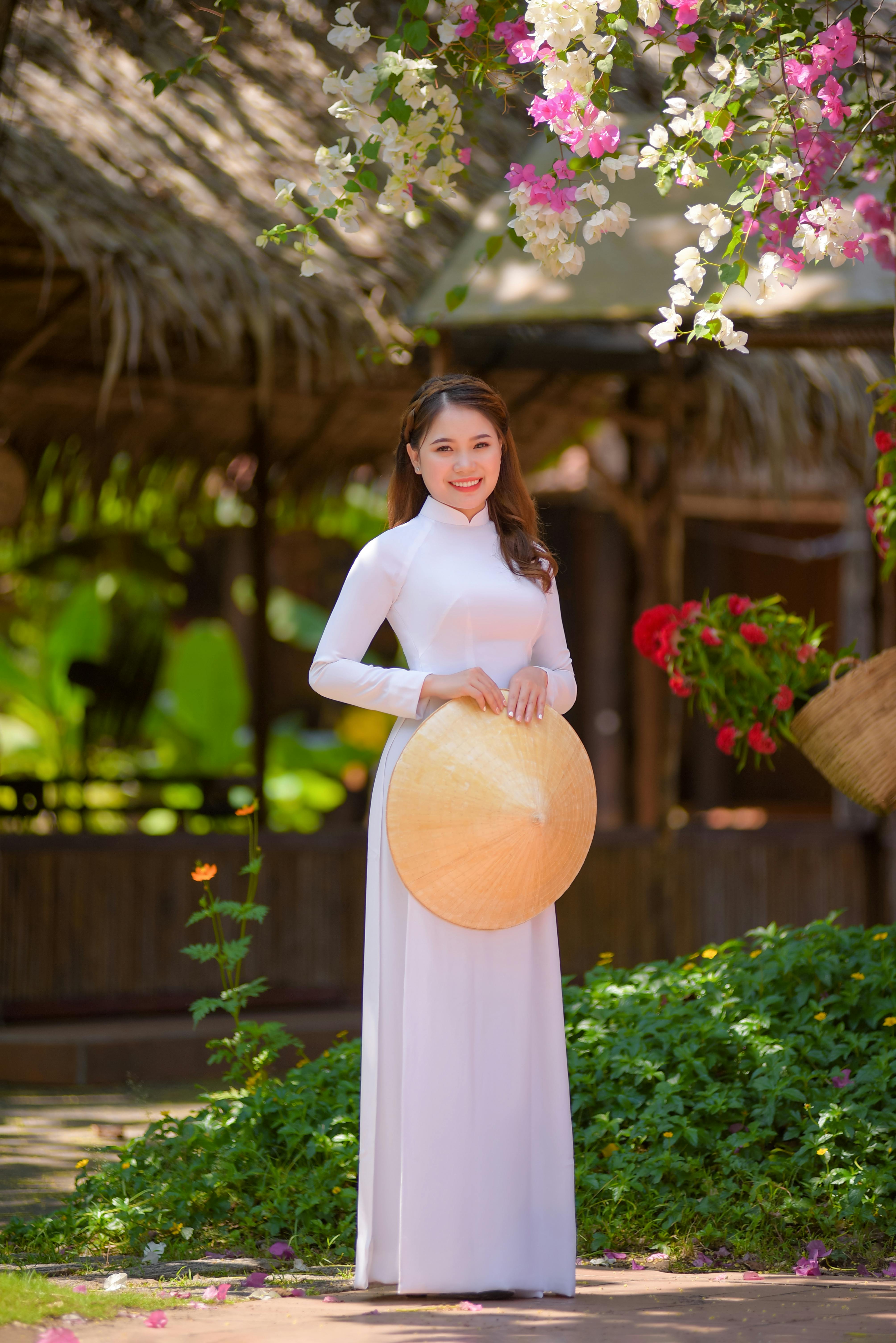 Elegant woman in ao dai and straw hat smiling in a vibrant Vietnamese garden.