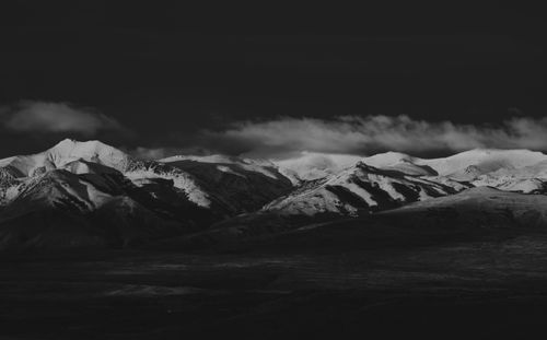 Free Monochrome aerial view highlighting a snowcapped mountain range under shadowy clouds. Stock Photo