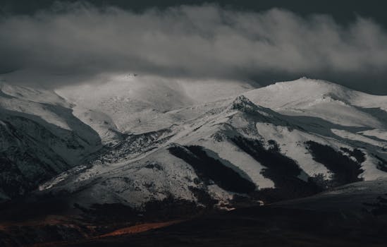A breathtaking view of snow-covered mountains under a cloudy sky with a dramatic atmosphere.