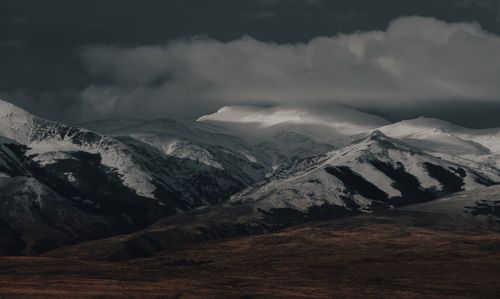 Free A dramatic snow-covered mountain range beneath a dark, cloudy sky, showcasing rugged natural beauty. Stock Photo