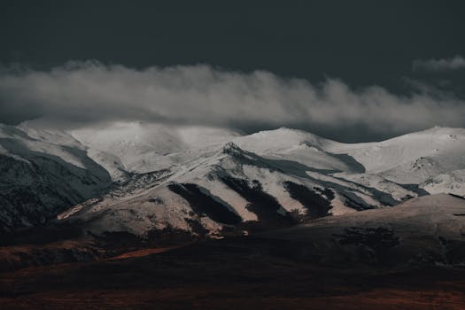 Breathtaking view of snow-covered mountains under dramatic clouds at twilight.