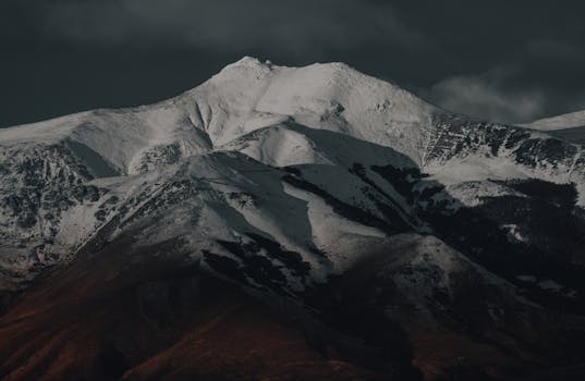 Dramatic snow-covered mountain peak under a moody dark sky, showcasing nature's majesty.