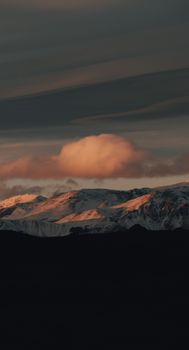 Serene snow-capped mountains under a dramatic sunset sky, showcasing nature's beauty.