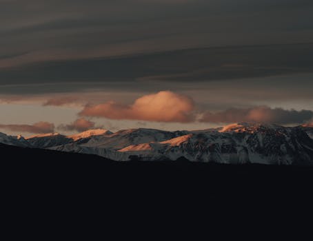 A breathtaking view of snow-capped mountains under a dramatic sunset sky.