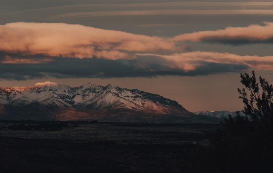 Dramatic view of snow-capped mountains under a moody sky as twilight sets in.