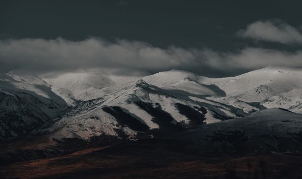 Breathtaking view of snow-capped mountains under dark clouds, perfect for nature lovers.