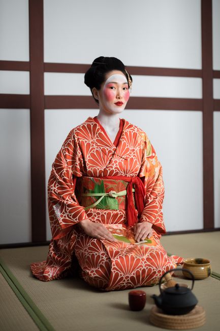 Elegant geisha in kimono performs traditional Japanese tea ceremony indoors.