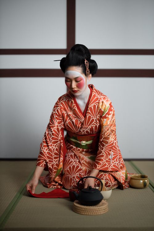Free A geisha in a kimono performing a traditional Japanese tea ceremony indoors. Stock Photo