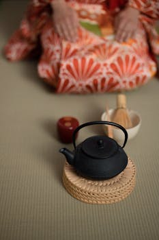 Traditional Japanese tea ceremony with a focus on a black teapot and vibrant kimono.