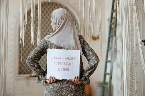Free A woman in a hijab holds a sign promoting women's solidarity indoors. Stock Photo