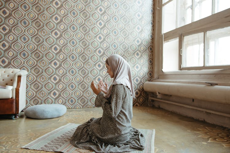 Woman In Long Dress And Headscarf Praying On A Rug