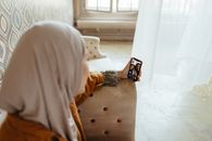 A woman in a hijab using a smartphone for a video call in a cozy indoor setting.