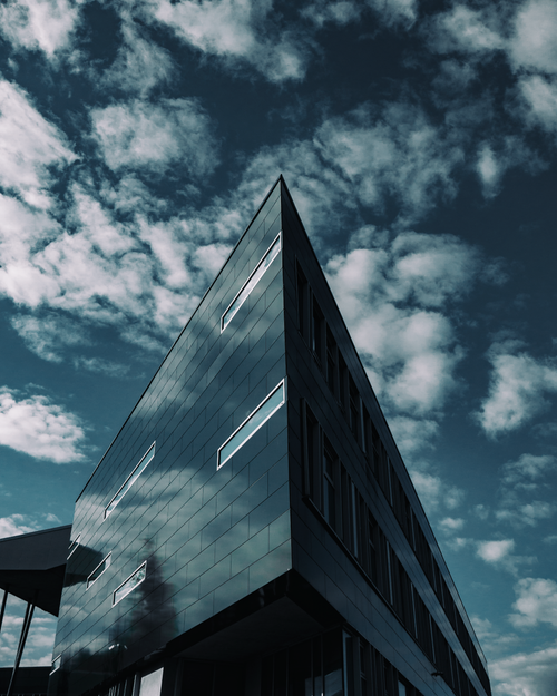 Free A striking contemporary building with a sleek facade reflecting the cloudy sky. Stock Photo