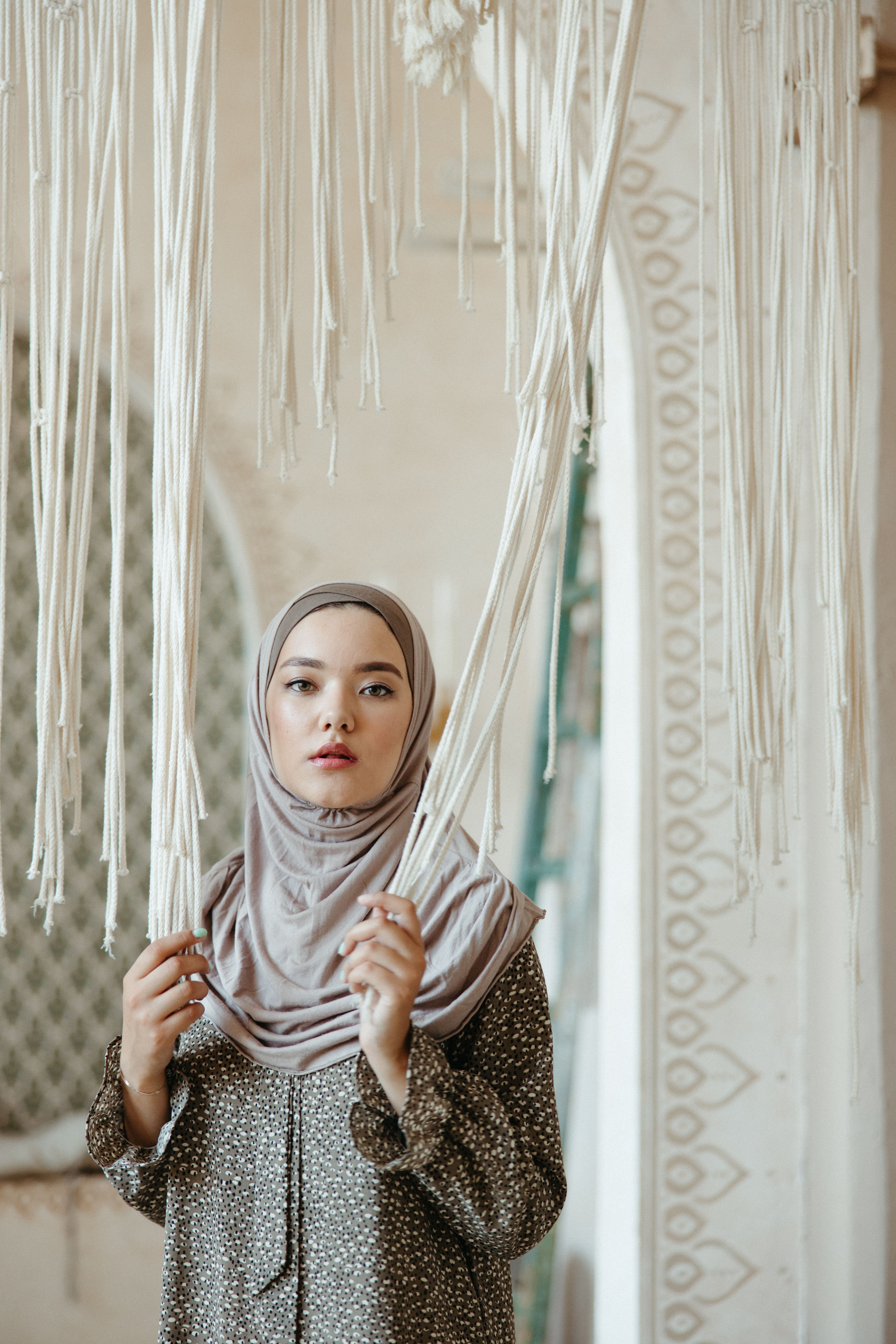 Woman in Brown Dress and Hijab Holding a Curtain · Free Stock Photo