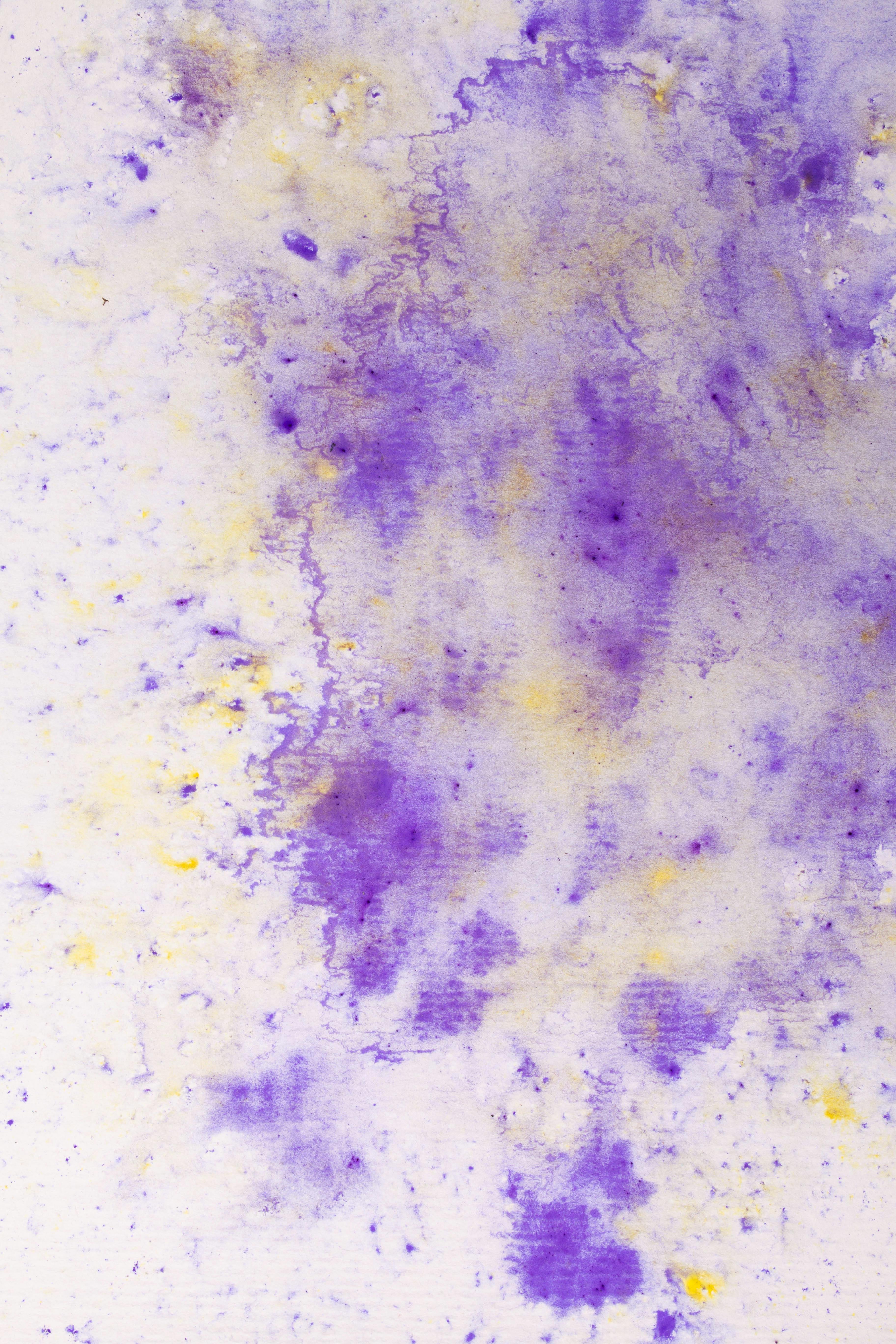Abstract watercolor texture with vibrant purple and yellow splashes on paper.